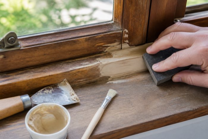 Wooden window frame being repaired with sanding tools and filler